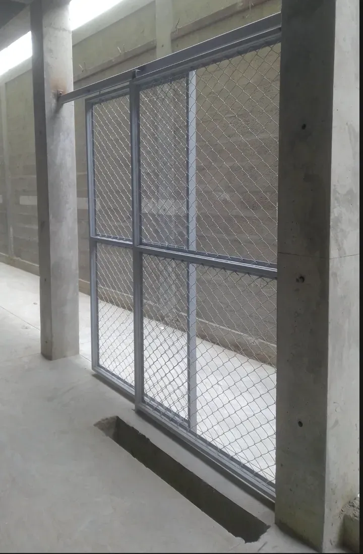 Cerramiento metálico corredero con bastidor de perfil y malla de simple torsión entre pilares de hormigón