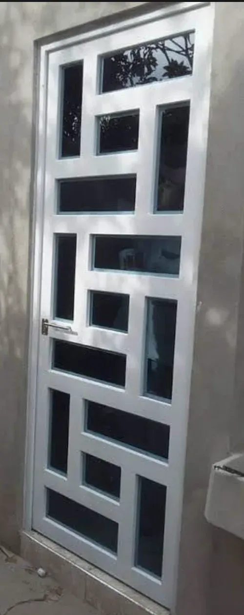 Puerta metálica acristalada con despiece rectangular irregular, instalada en un hueco de obra